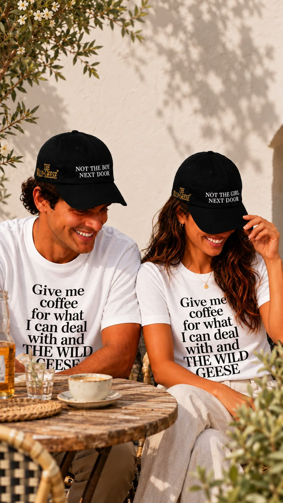 Couple at a cafe in The Wild Geese caps and Give Me Coffee T-shirts
