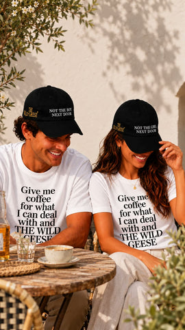 Couple at a cafe wearing The Wild Geese Give Me Coffee white t-shirts and Not the Boy / Not the Girl Next Door black caps